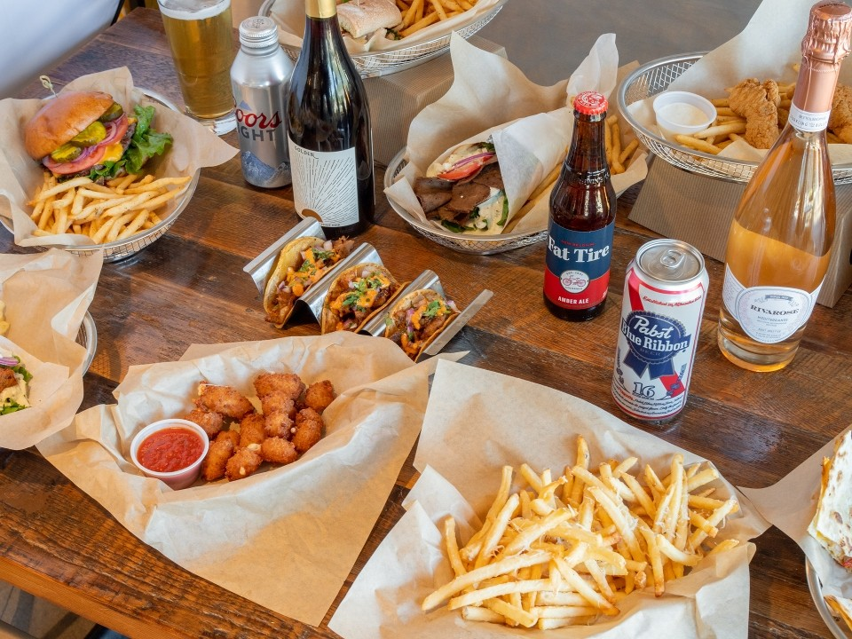 A table filled with Wild Plum sandwiches, tacos, appetizers, fries, beer, wine, and sparkling wine